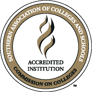 Three golden, angled, wavy lines representing a torch with the stacked words Accredited Institution in black, capitalized letters centered below it on a white circle. A golden ring lies just inside the outer edge of the circle with the words Southern Association of Colleges and Schools in white, capitalized letters on the upper 3/4s and the words Commission on Colleges in black, capitalized letters on the lower 1/4.