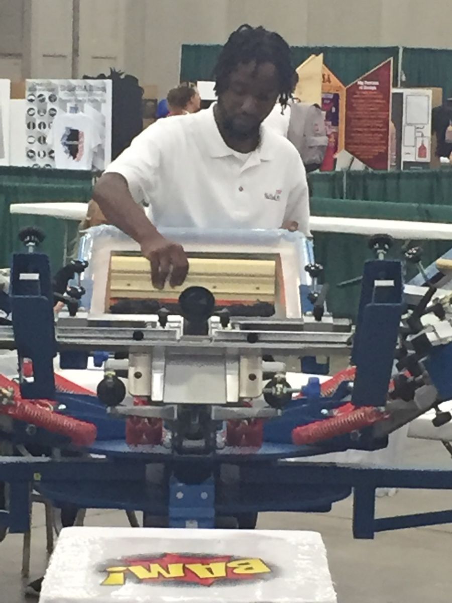 Young African American college student in white polo shirt, James McRae, works on screen printing during the competition.