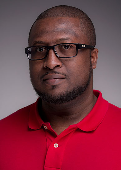 An African American male with a beard, Dederick Scott wears a red collared polo and black rimmed glasses.