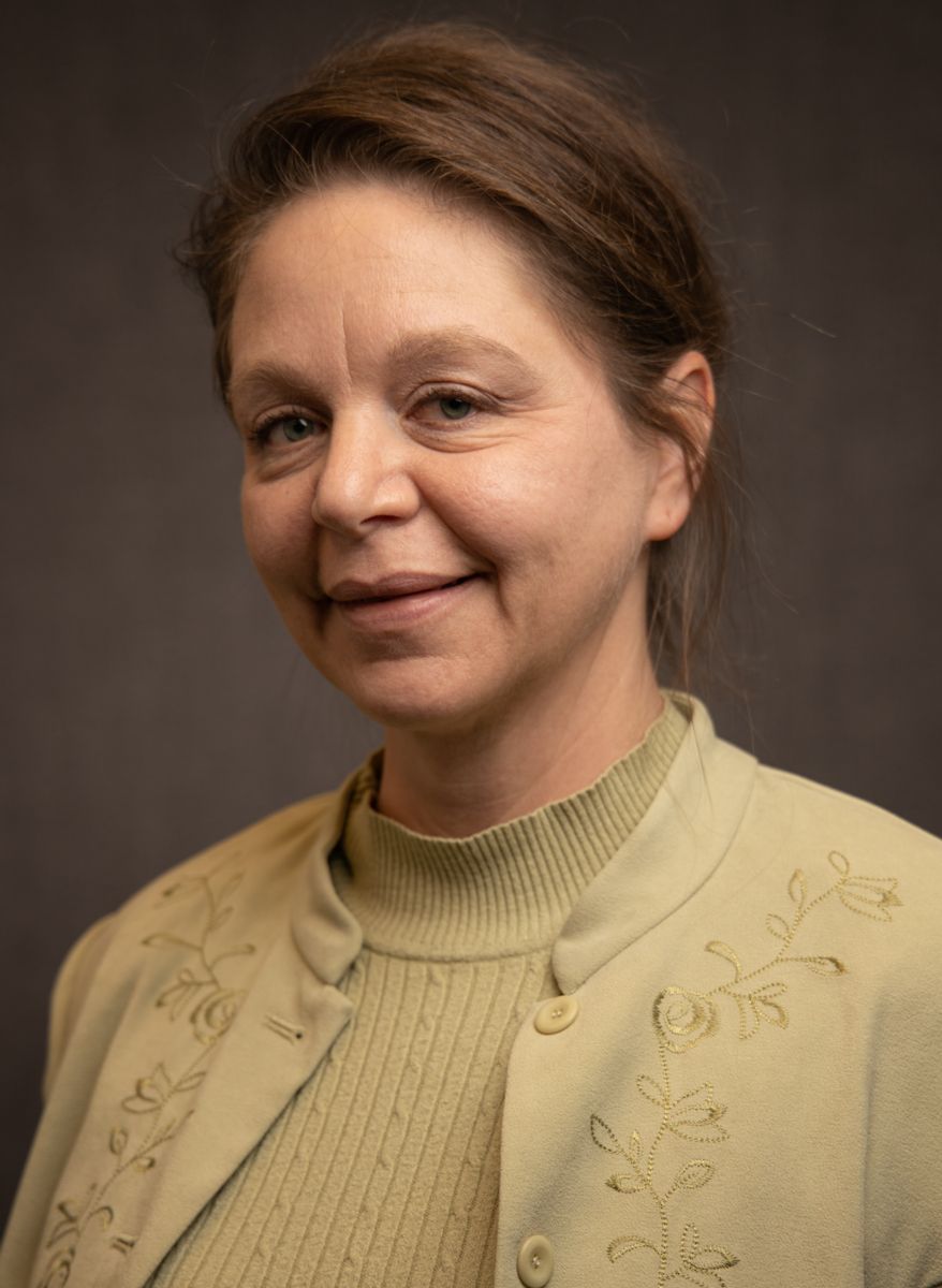 A Caucasian female with brown hair, Vianne Prowse is wearing a gold sweater as well as a gold dress jacket with flowered vine decorations running from the shoulder, across the chest area, down to the hem and a button enclosure.