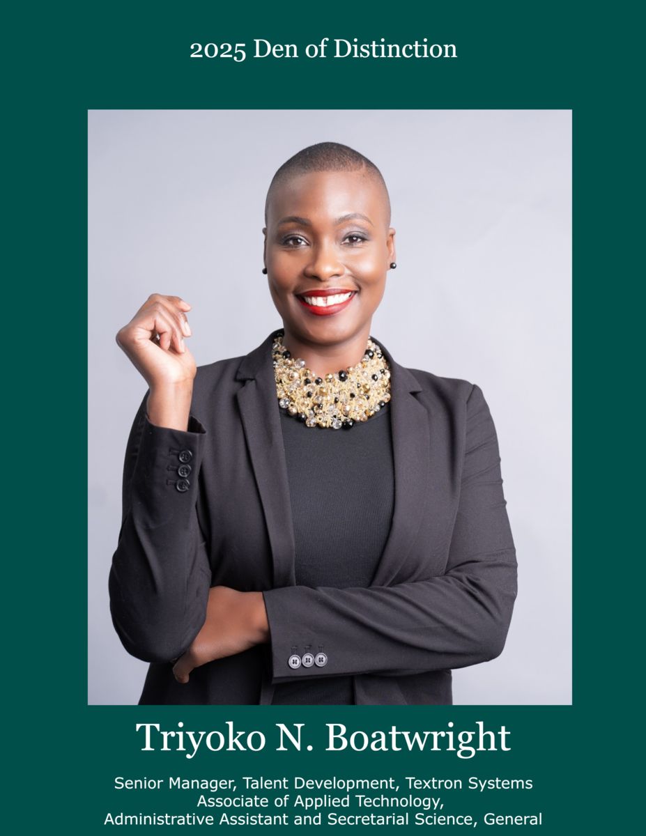 Triyoko N. Boatwright, an African American female, smiles at the camera wearing a charcoal suit jacket over a charcoal dress with a multilayered gold necklace interspersed with black beads.