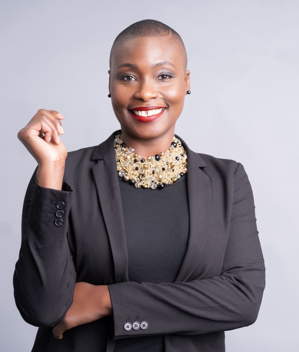 Triyoko N. Boatwright, an African American female, smiles at the camera wearing a charcoal suit jacket over a charcoal dress with a multilayered gold necklace interspersed with black beads.