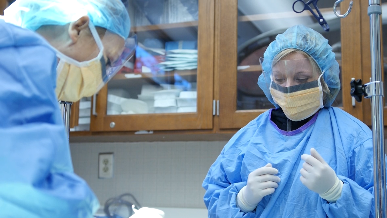 Two students dressed in scrubs and masks practice surgical techniques.