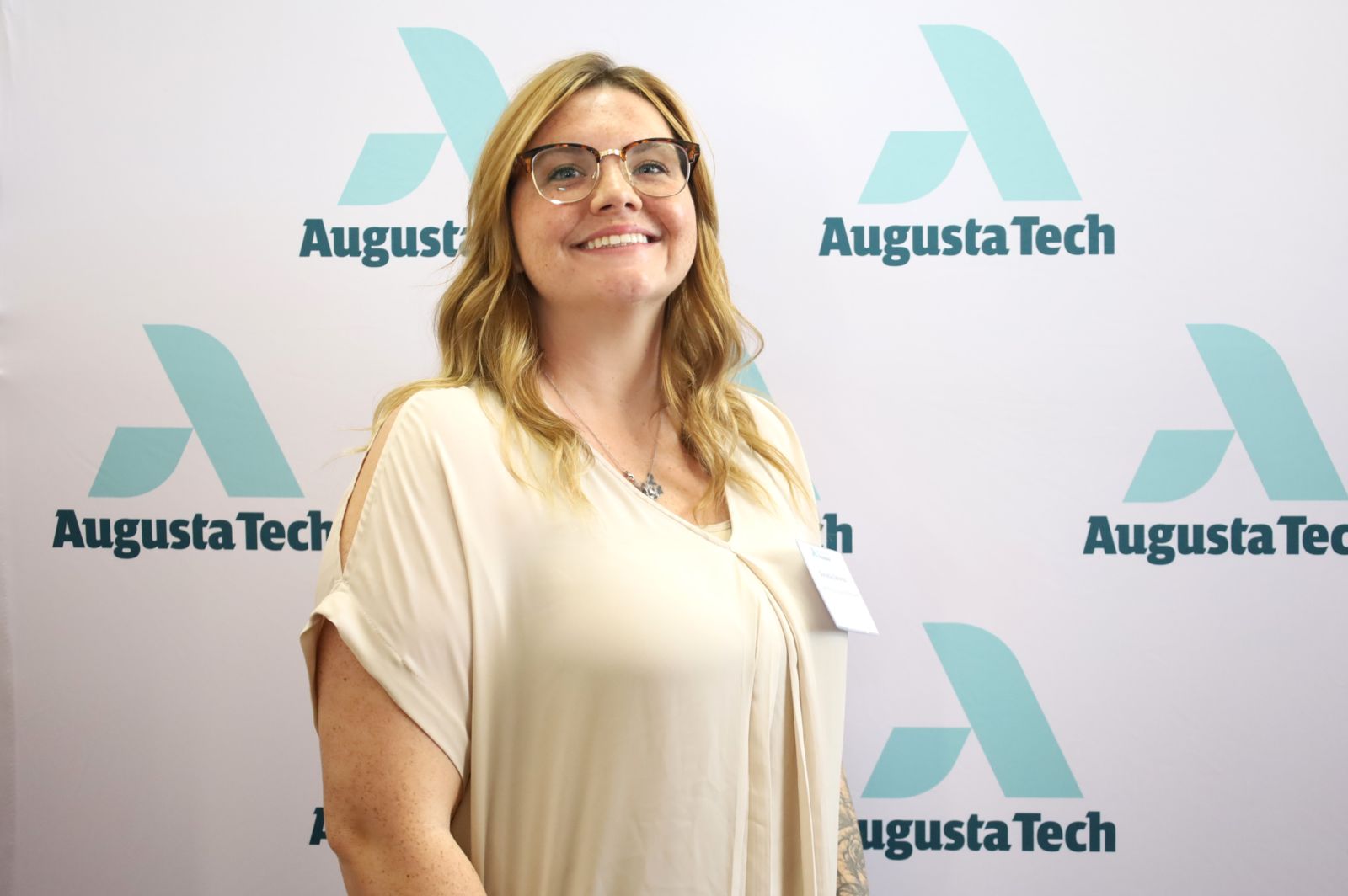 Danielle Zerona, a Caucasian female with long blonde hair, smiles at the camera wearing a cream dress shirt. Pictured against a backdrop featuring the Augusta Tech icon in Mint Green above the words Augusta Tech in heritage green displayed five times.