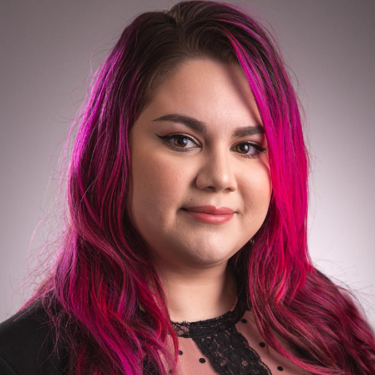 Caucasian woman with dark brown and pink hair wearing a black and brown polka dot shirt, posing for a photo