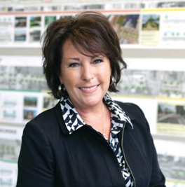 Smiling, Caucasian female with brown hair, wearing silver earrings, a blue zippered jacket with blue and white collared shirt and a silver necklace posing for a photo