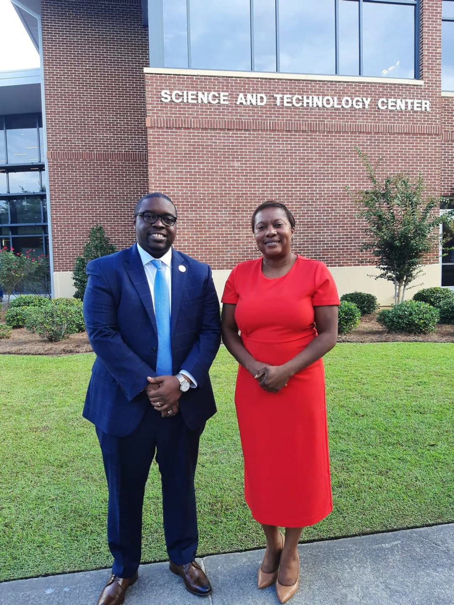 Dr. Jermaine Whirl, an African American male smiles wearing black rimmed glasses, a navy suit with a light blue tie and white shirt stands beside Kimberly Ballard-Washington, J.D., an African American Female, who is also smiling wearing a red dress. The two stand in front of the Science and Technology Center