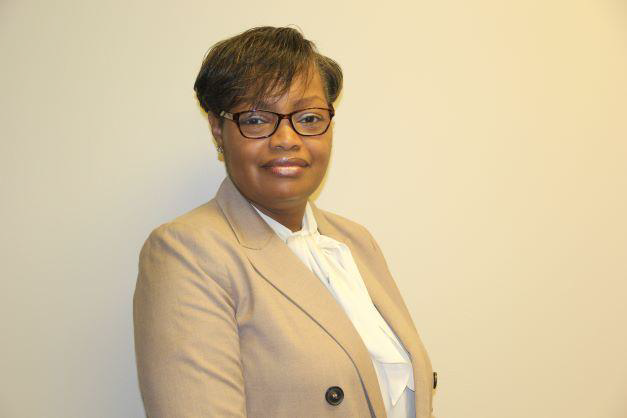 African American female wearing a black glasses, tan blazer with black button, and white shirt posing for a photo