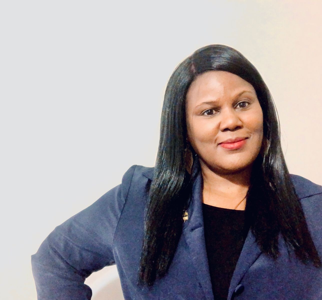 Smiling African American girl with long black hair, wearing red lipstick, gold leaf earrings, wearing a blue blazer with a gold lapel pin and a black undershirt.