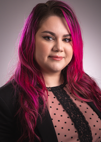 Caucasian female with long pink hair, wearing a black blazer and pink and black shirt with black polka dots and black lace