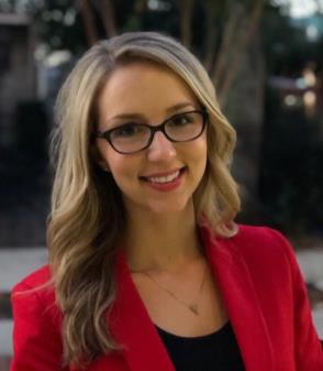 Ms. Marissa Smith, a Caucasian female with long blond hair wears black rimmed glasses and a black suit jacket with a white shirt while smiling at the camera.