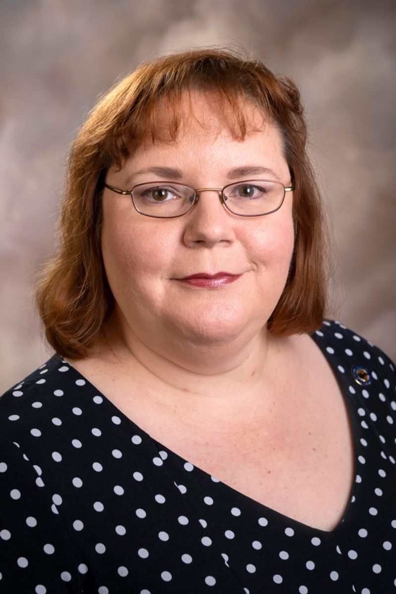 Mrs. Cheryl Ciucevich, a Caucasian female with shoulder length red hair, smiles wearing a black and white polka dot dress.