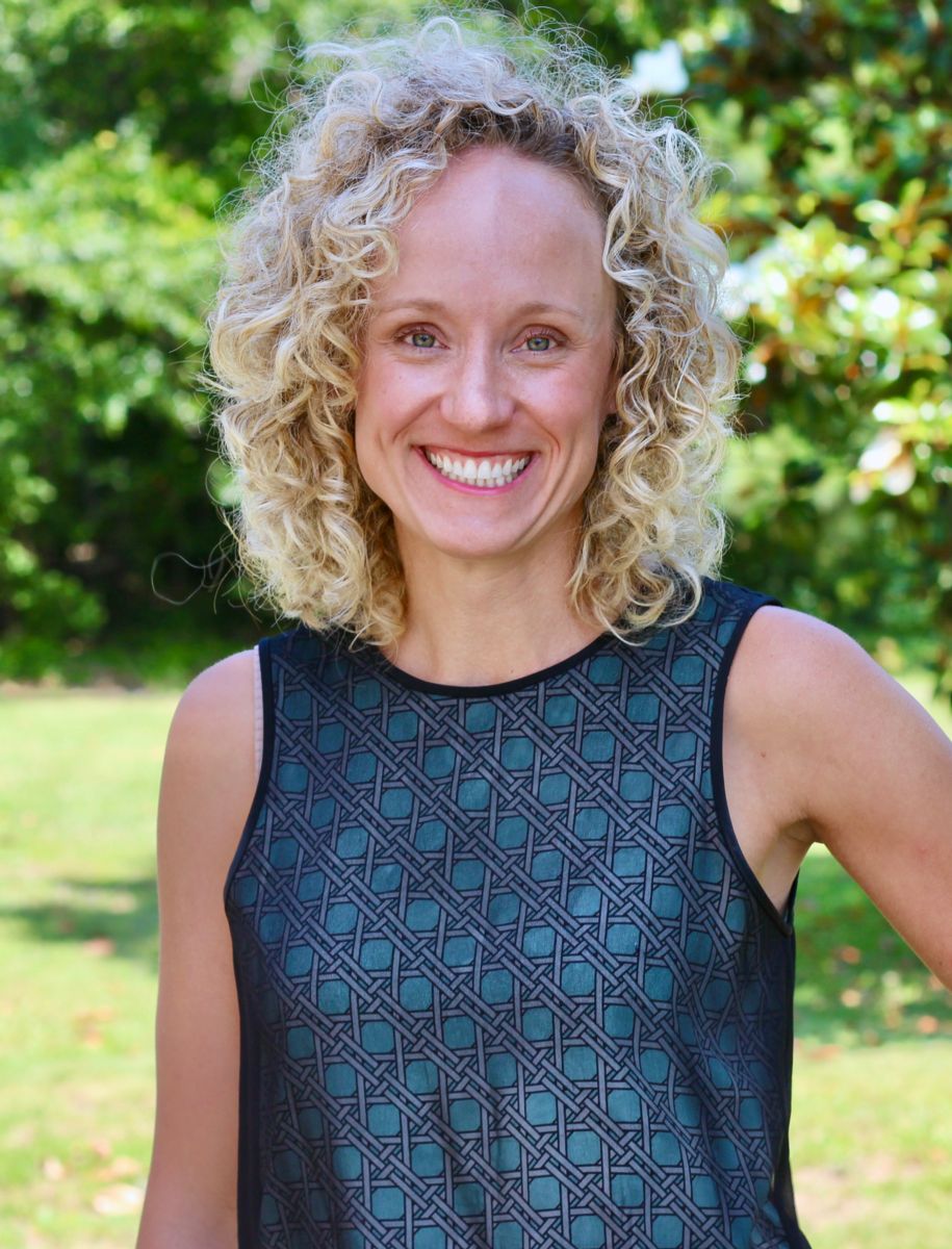 Ms. Jane Marie Kinsey, a Caucasian female with curly blonde hair smiles wearing a dark green dress with a grey lattice pattern.