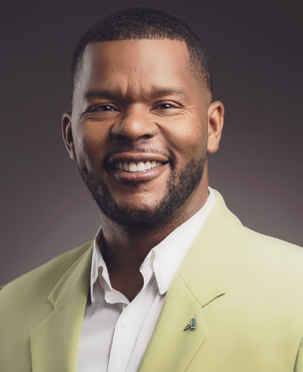 Dr. Ken Blair, an African American male, smiles at the camera wearing a yellow suit jacket with a white collared shirt.