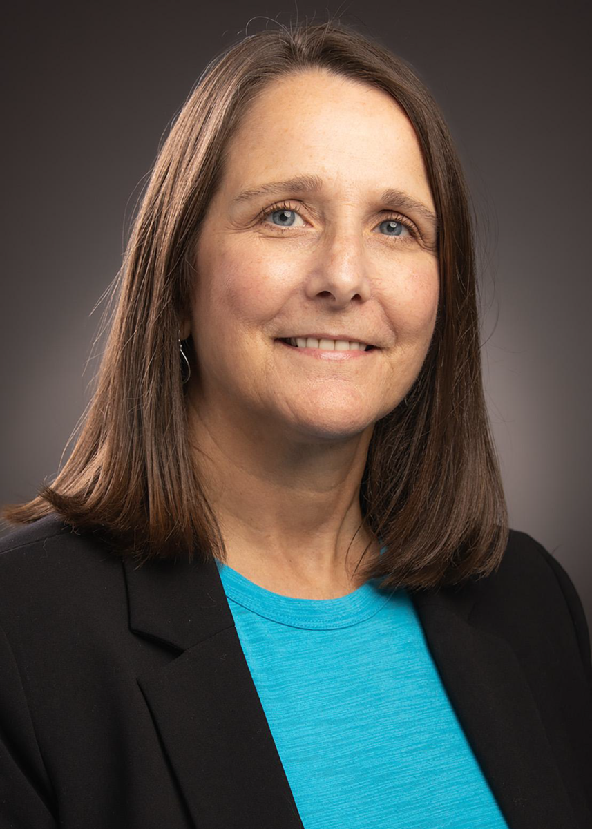 LeAnne Lovering, a Caucasian female with shoulder length light brown hair, smiles at the camera wearing a black suit jacket and turquoise shirt.