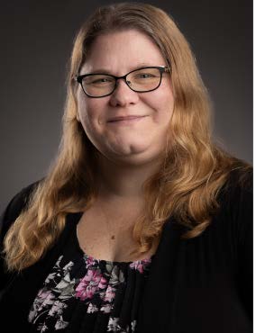 Headshot of Dr. Melissa Frank-Alston smiling, with shoulder-length gray hair, wearing a royal blue outfit and pearl earrings against a plain gray background.
