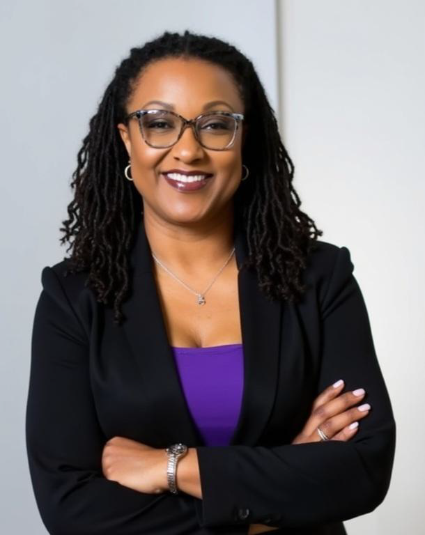 Dr. Lillian Williams, an African American female with long curly hair, smiles at the camera wearing a black suit jacket over a purple dress with small hoop earrings, a watch and glasses.