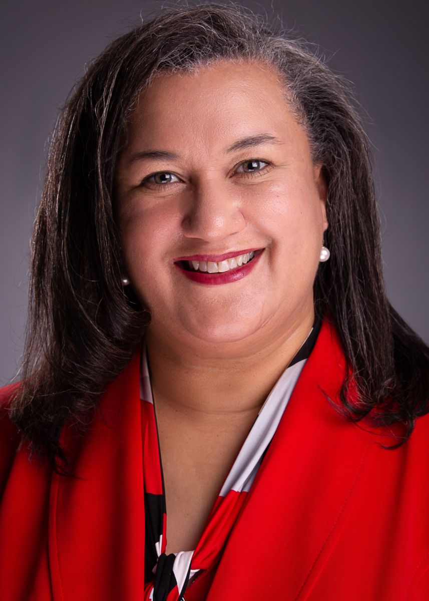 Smiling, Caucasian woman wearing white pearl earrings, red blazer, and a red, black, and white scarf posing for a photo.
