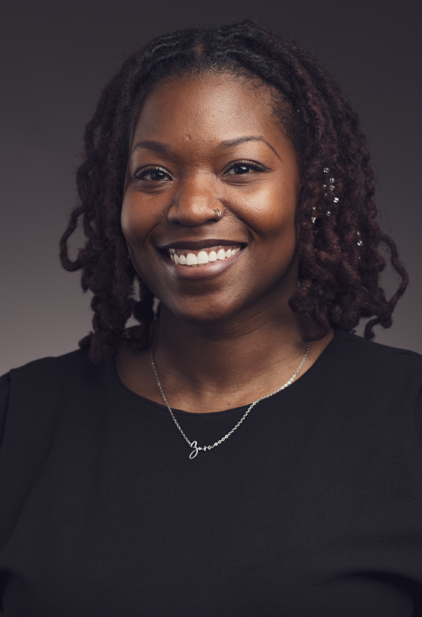 Ms. Zuri Todd, an African American female with shoulder length braided brown hair, smiles at the camera wearing a black shirt.