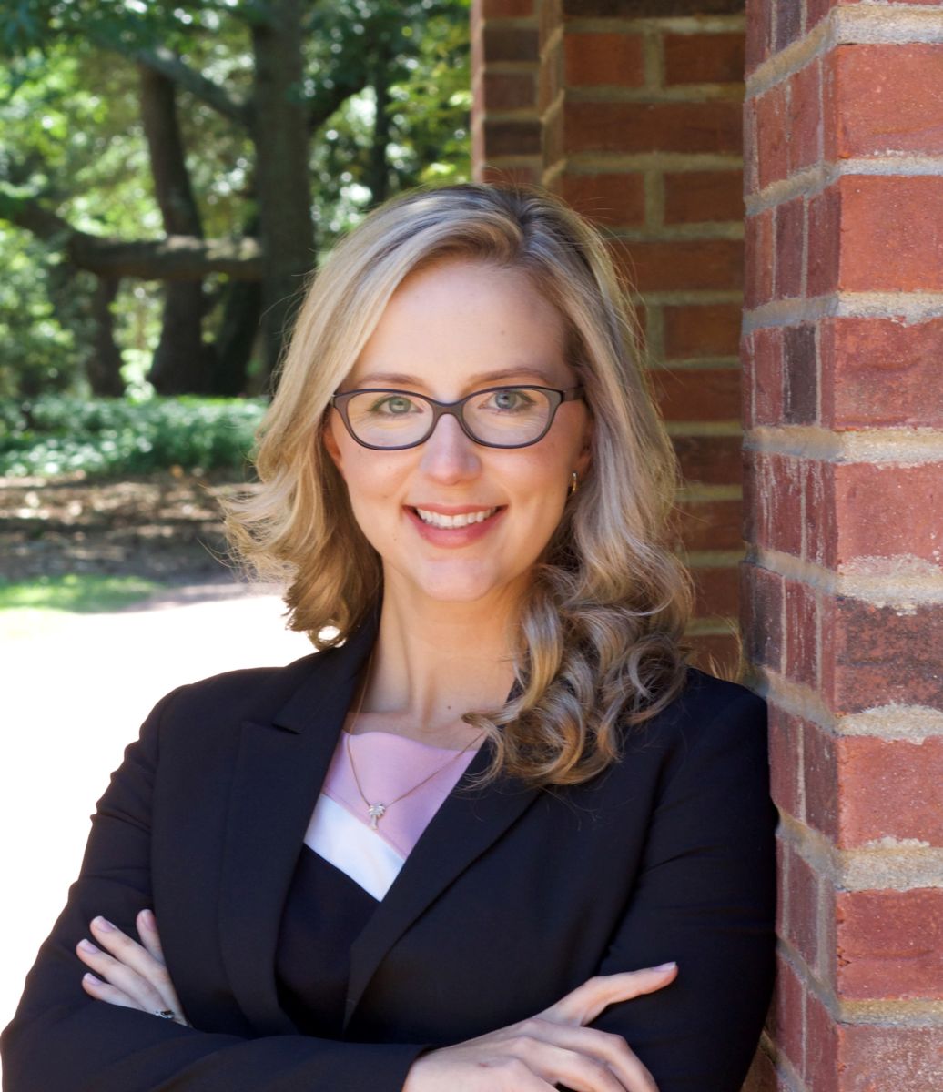 Ms. Marissa Smith, a Caucasian female with long blond hair wears black rimmed glasses and a black suit jacket with a white shirt while smiling at the camera.