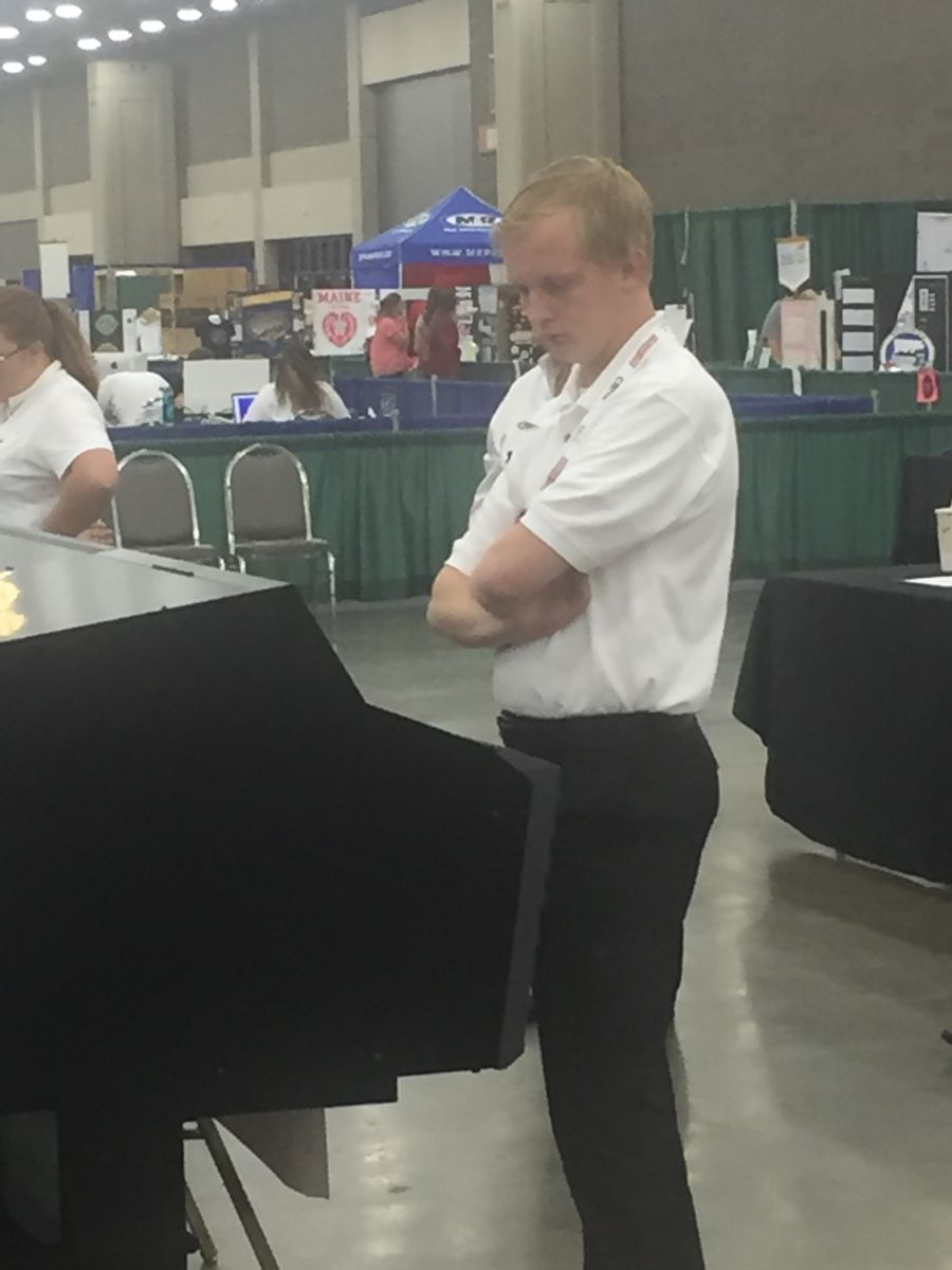 A young Caucasian college student in a white polo shirt and black dress pants, Hunter Steed, stares down at a graphics display during the competition.